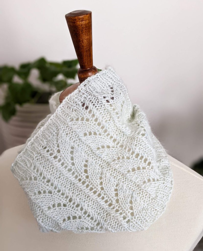 A very pale mint green cowl with an arrow-shaped lace pattern is placed around the neck of a white dressmaker's form.