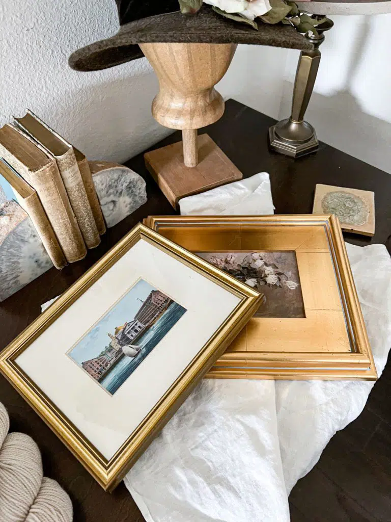 A top-down view of two prints framed in gilded frames sitting on a dark brown desk.