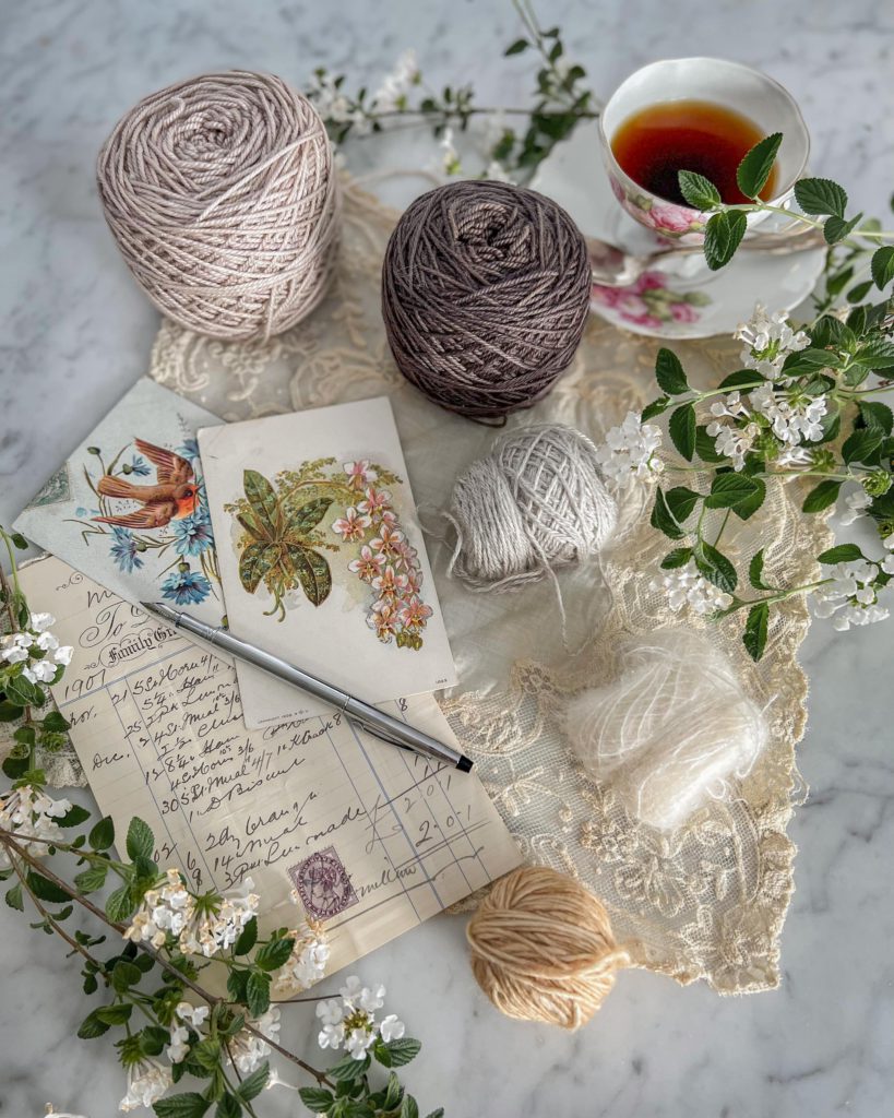 Five balls on yarn in descending size order curve from top to bottom around antique paper ephemera and a pink and white teacup