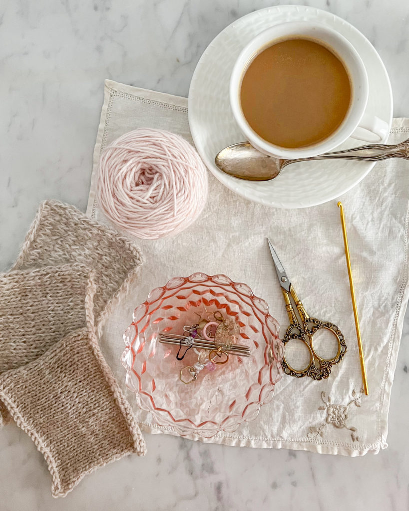 A top down shot of a collection of knitting tools, including scissors, stitch markers, and a crochet hook.