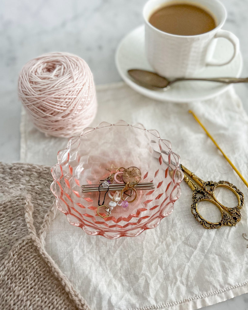 A side-angle shot of a collection of knitting tools, including scissors, stitch markers, and a crochet hook.