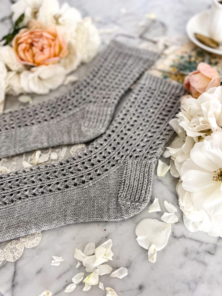 A close-up on the heels of a pair of gray, lacy socks laid out flat on a white marble counter.