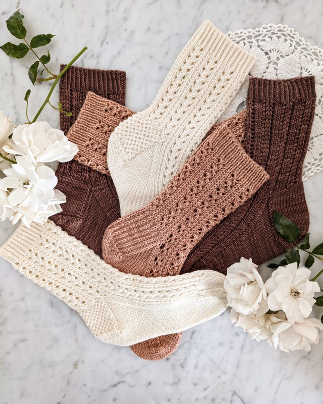 A jumbled pile of three pairs of lacy socks in cream, pink, and brown.