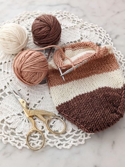 A close-up on the toe of a half-finished sock in brown, cream, and pink stripes. This month, I am learning to knit toe-up socks.