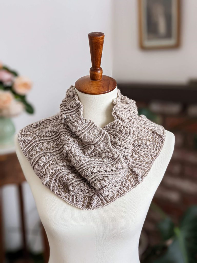 A highly textured gray cowl with lots of bobbles and lace is draped on a white dressmaker's form. Photographing your knits in a vertical space requires different considerations from photographing them on a flat surface.