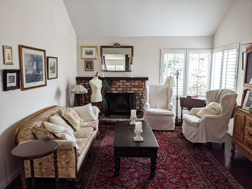 A pulled-out photo of my front room showing a sofa to the left, a brick fireplace on the back wall, two windows in the corners on the right, two slipcovered armchairs, a red Persian rug, and a dark brown coffee table. There is a dressmaker's form in the back left corner, opposite the windows. When photographing your knits, pay attention to where your light sources are.