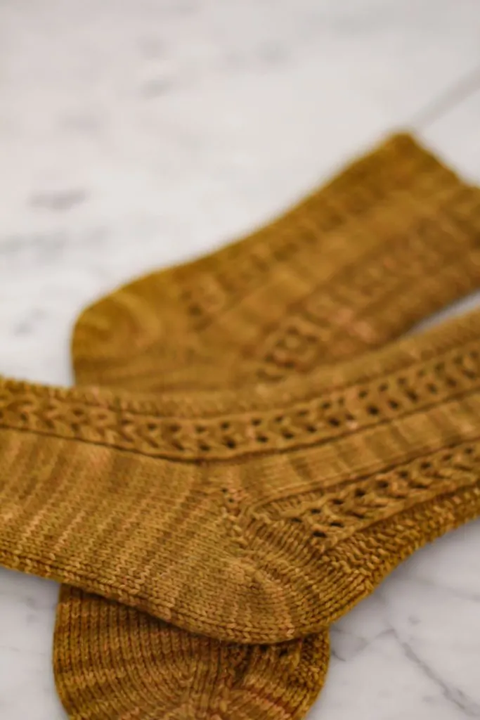 A pair of caramel-colored socks is laid out on a white surface. The image is focused on the short-row heel construction of the top sock.