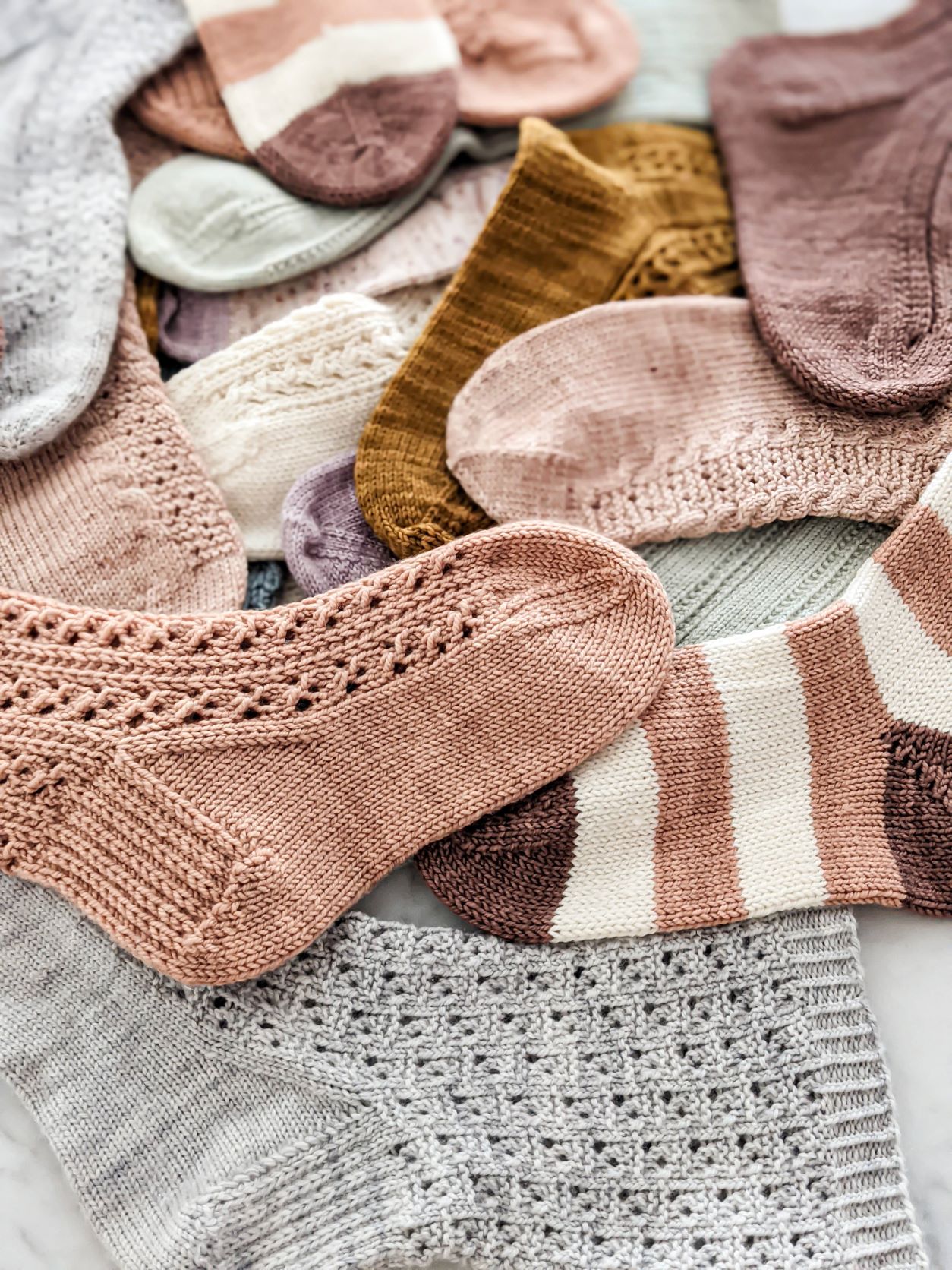 A pile of pink, brown, mint, blue, purple, and striped socks in all different styles laid out flat on a countertop.