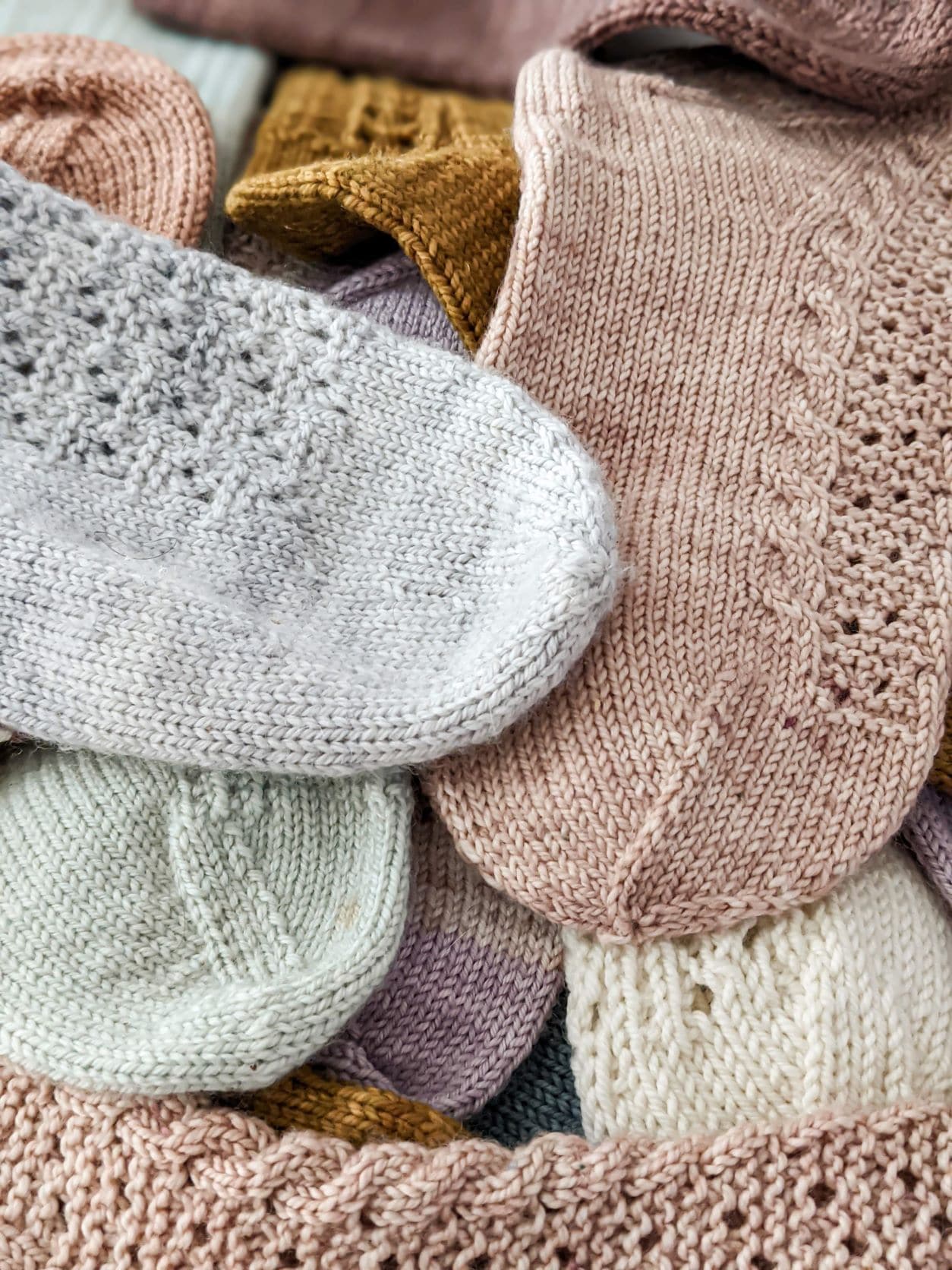A pile of pastel colored socks jumbled together. The image is zoomed in on a pale blue sock with a round toe, a pale pink sock with a star toe, and a pale green sock with a wedge toe.