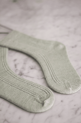 A pair of pale green socks with wedge toes laid flat on a white marble surface. The toes point toward each other.