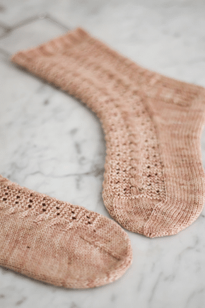 A pair of pale pink socks with star toes are laid flat on a white marble surface. The toes point toward each other.