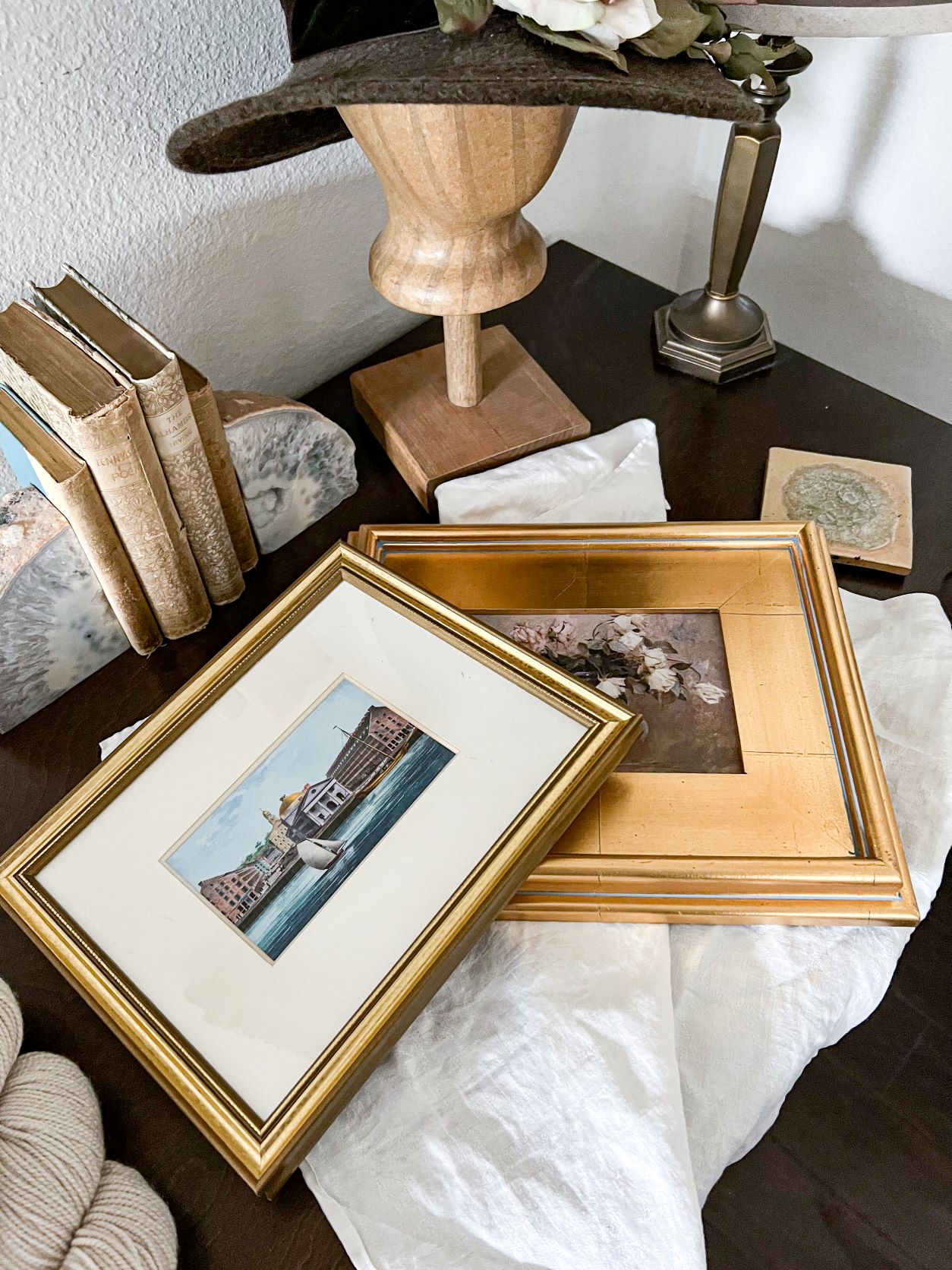 A top-down view of two prints framed in gilded frames sitting on a dark brown desk.