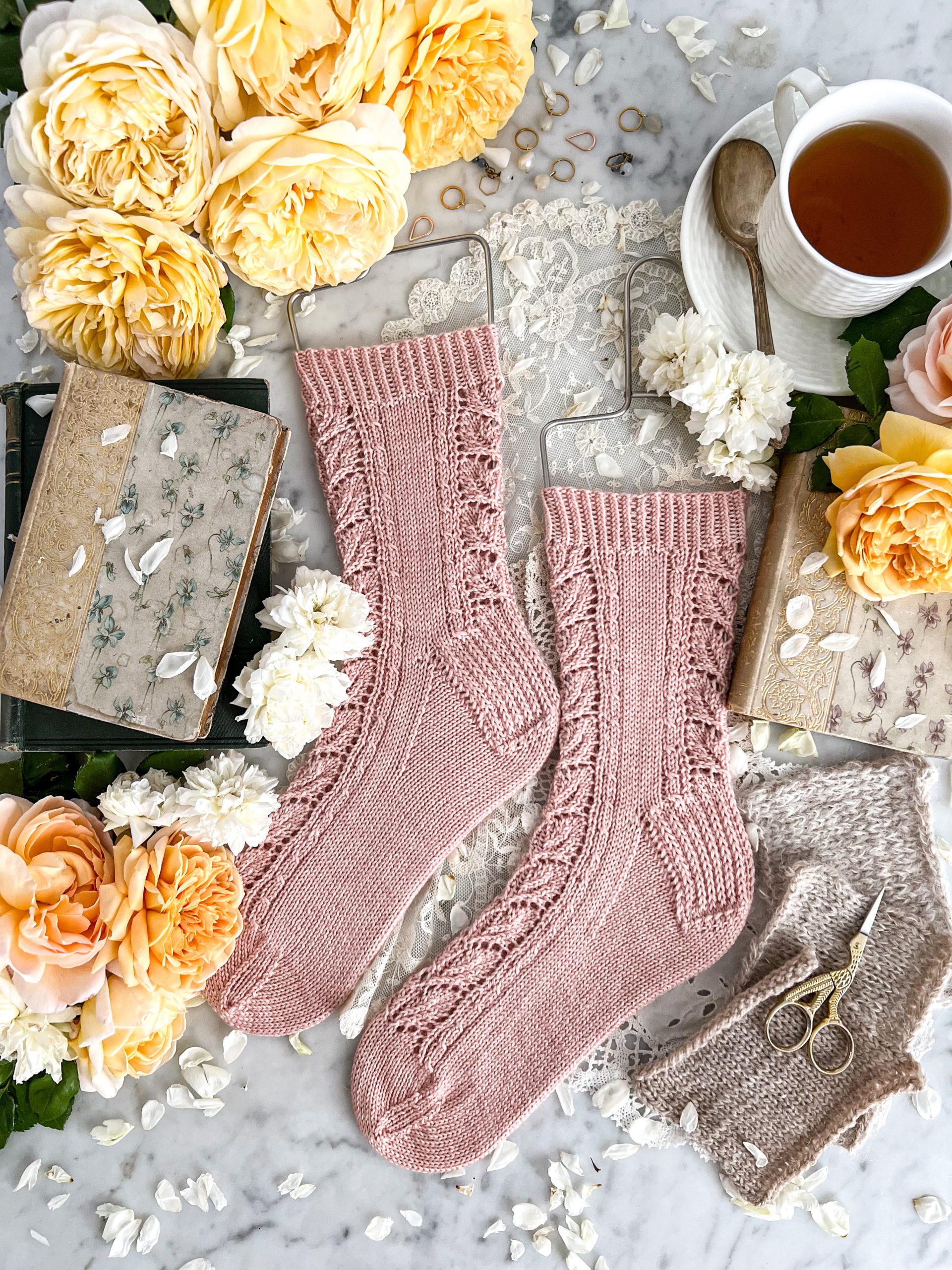 A top-down image of the Pyrifera Socks, a pair of pink socks with 1x1 twisted rib cuffs and lacy leaf panels down the front and back.