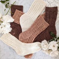 A jumbled pile of three pairs of lacy socks in cream, pink, and brown.