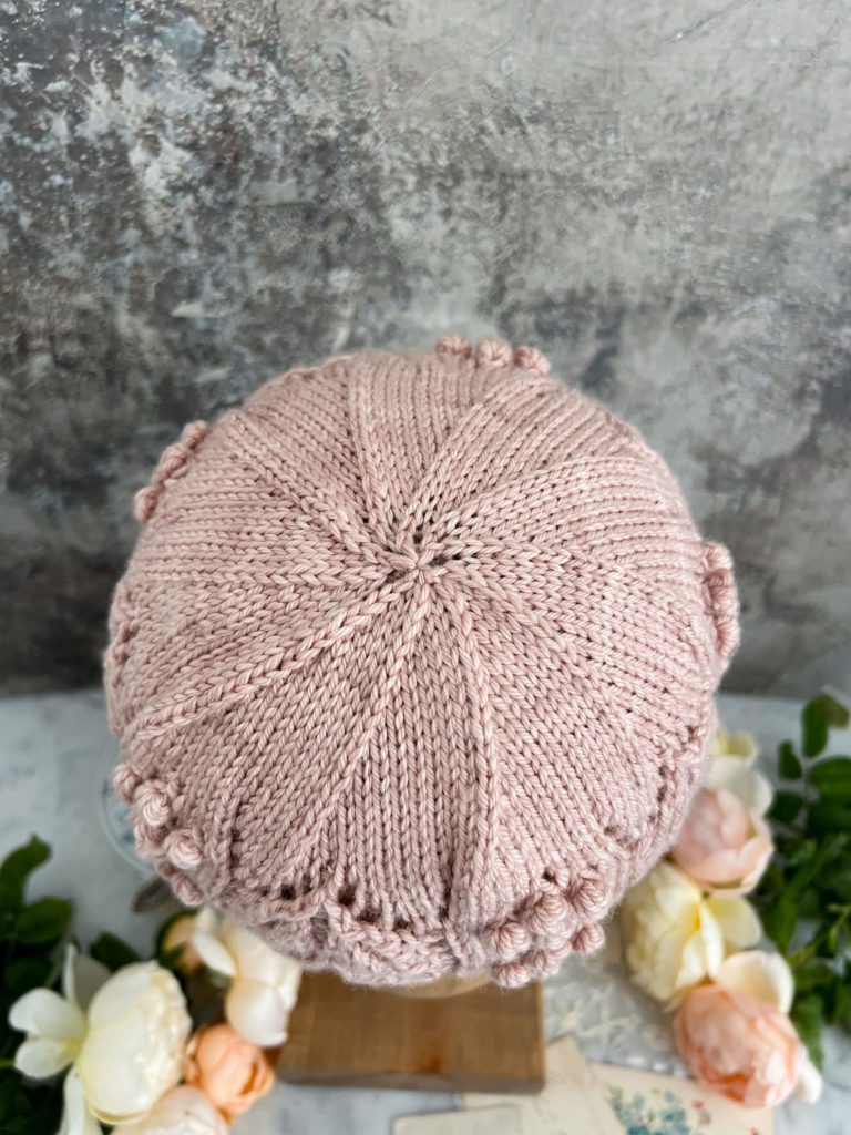 A top-down image of the crown of the Laurel Hat. The hat is pink, and the decreases of the crown cause it to look like it's spiraling.