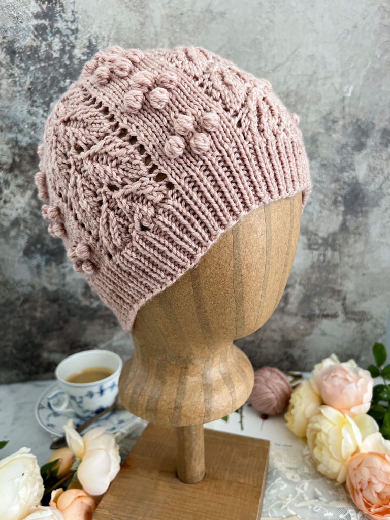 A 3/4 profile image of the Laurel Hat on a plain brown mannequin head. The image shows what the bobbles and lacy leaves look like opened up on a head instead of laid flat on a surface.