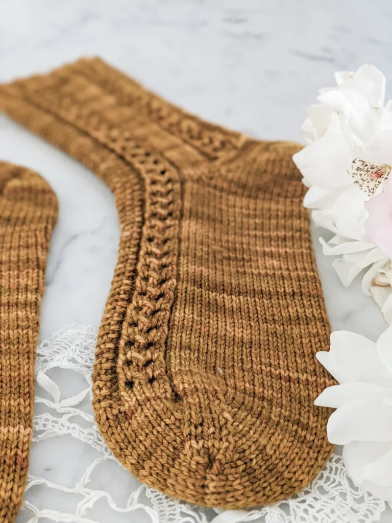 A close up on the toes of one of the Creme Brulee Socks, a caramel-colored sock with eyelet and seed stitch panels.