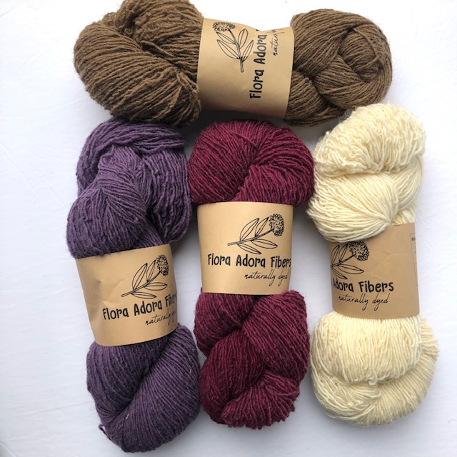 Four skeins of naturally dyed yarn in shades of brown, cream, berry, and purple