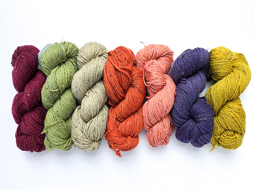 Seven skeins of naturally dyed tweed yarn in various shades of pink, blue, green, yellow, and purple.
