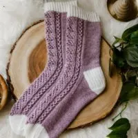 A pair of purple lacy socks with white cuffs, heels, and toes is laid out on a thin sliver cut from a tree trunk. The toes are pointing to the left.