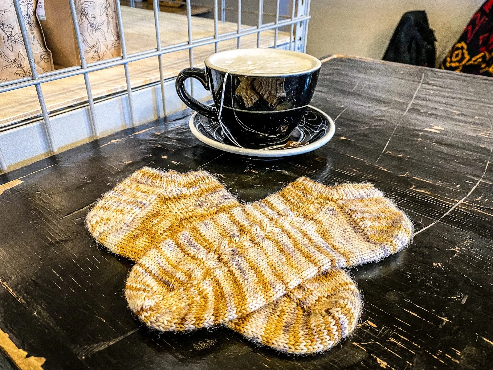 A pair of orange striped anklet socks is laid flat on a cafe table top with a cup and saucer full of frothy milk in the background.