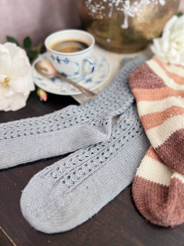 A pair of light blue lacy socks with significant pilling are laid out on a flat surface. To their right is a pair of brown, pink, and white socks that also have significant pilling.