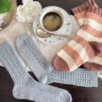 A top-down photo of the two pairs of socks featured in this post, one light blue and lacy, one with pink, white, and brown stripes. Both have had all their pills removed and look crisp and sharp again. Tucked in the middle between them is a blue and white teacup full of coffee and a white rose.
