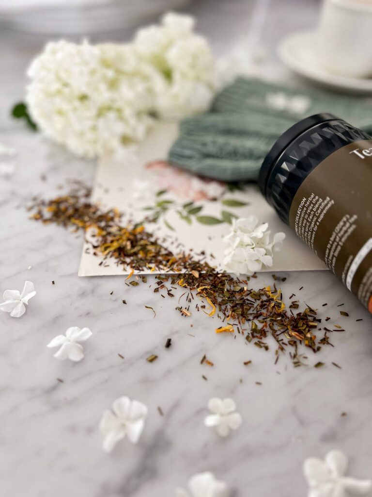 A bit of Tea Forte's Apricot Amaretto is scattered on a white marble countertop to show its texture. Blurred in the background are white flowers and the tops of some gray-green socks.