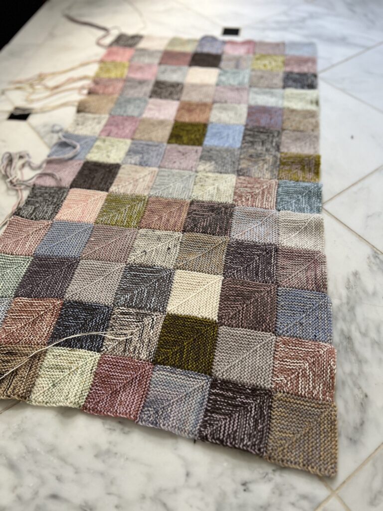 A zoomed-in photo of the lower right corner of a mitered square blanket in progress. There are pink, brown, blue, purple, and cream squares.