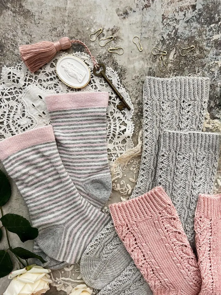 A close-up on the cuffs of some hand-knit and store-bought socks in shades of pink and gray.