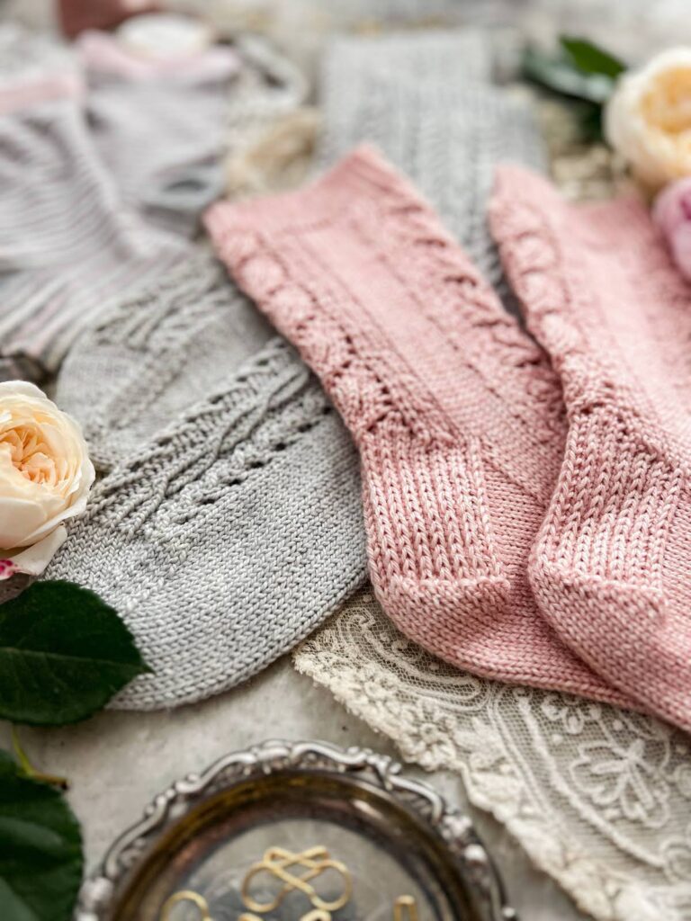 A close-up on the heels of a pair of pink hand-knit socks and the toes of a pair of gray hand-knit socks.