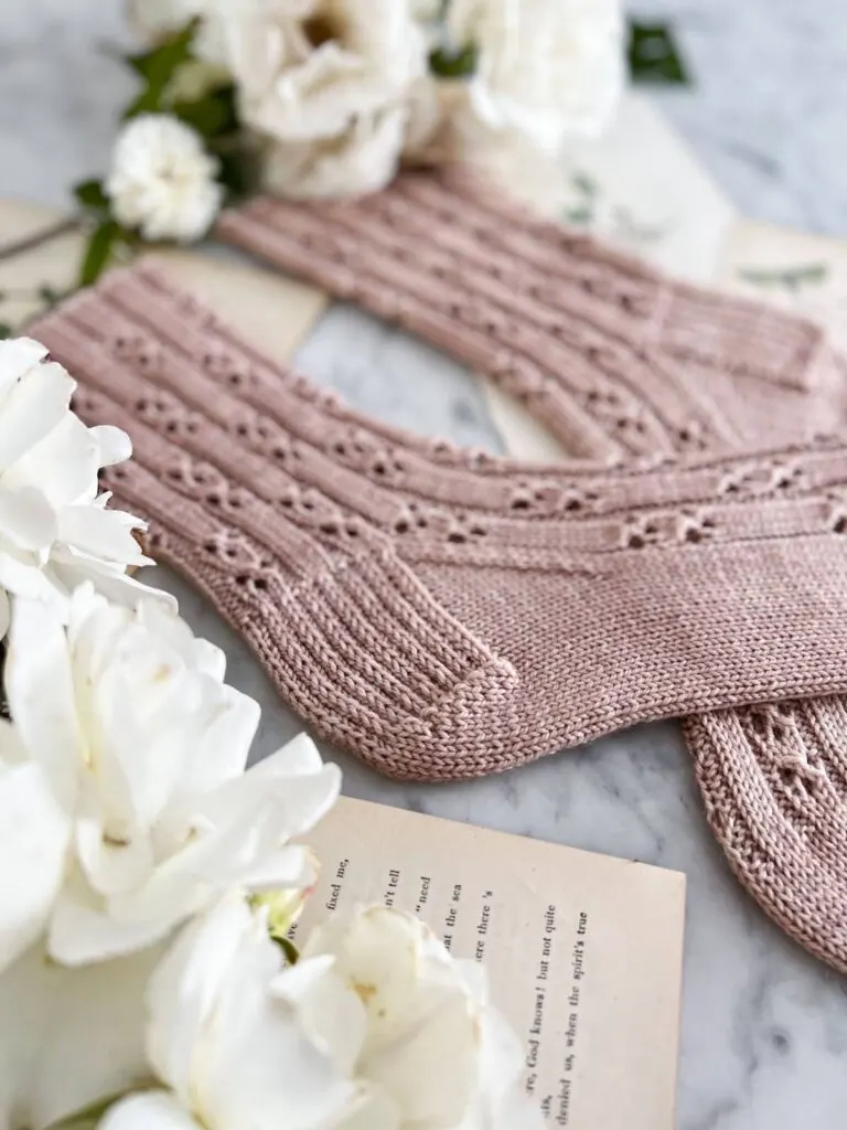 A detail shot of a pair of pink handknit socks showing the heel construction of the sock. The Baluster Socks feature a heel flap and gusset. The stitches of the heel are slipped for added cushioning and durability.