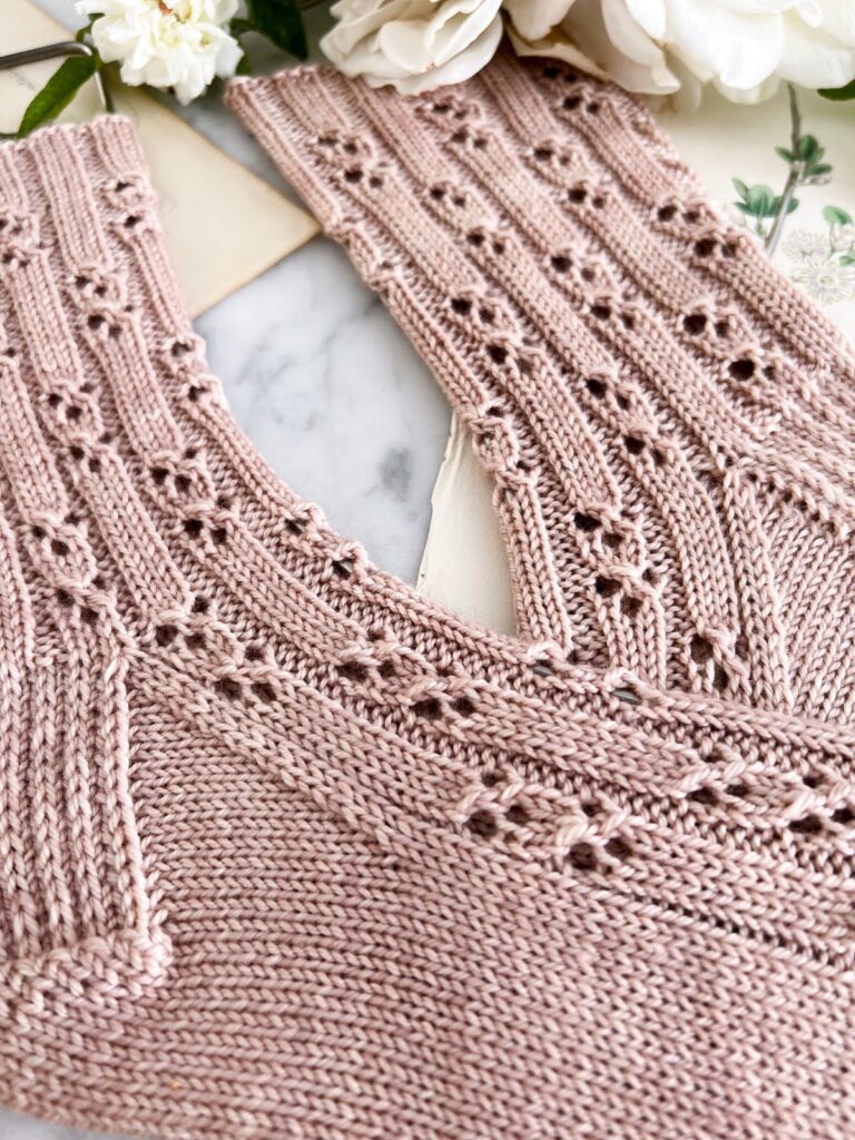 A close-up of the foot of a pink handknit sock with an all-over eyelet texture. This shows the eyelets in detail, including how they're staggered with ribbing between them and clustered into pairs with three stitches in each half of the pair.