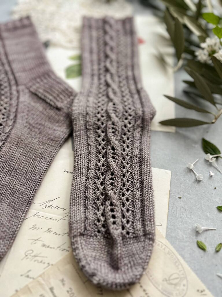 A close-up on the front panel of a grayish-purple sock. This shows the socks cables and eyelets in more detail.
