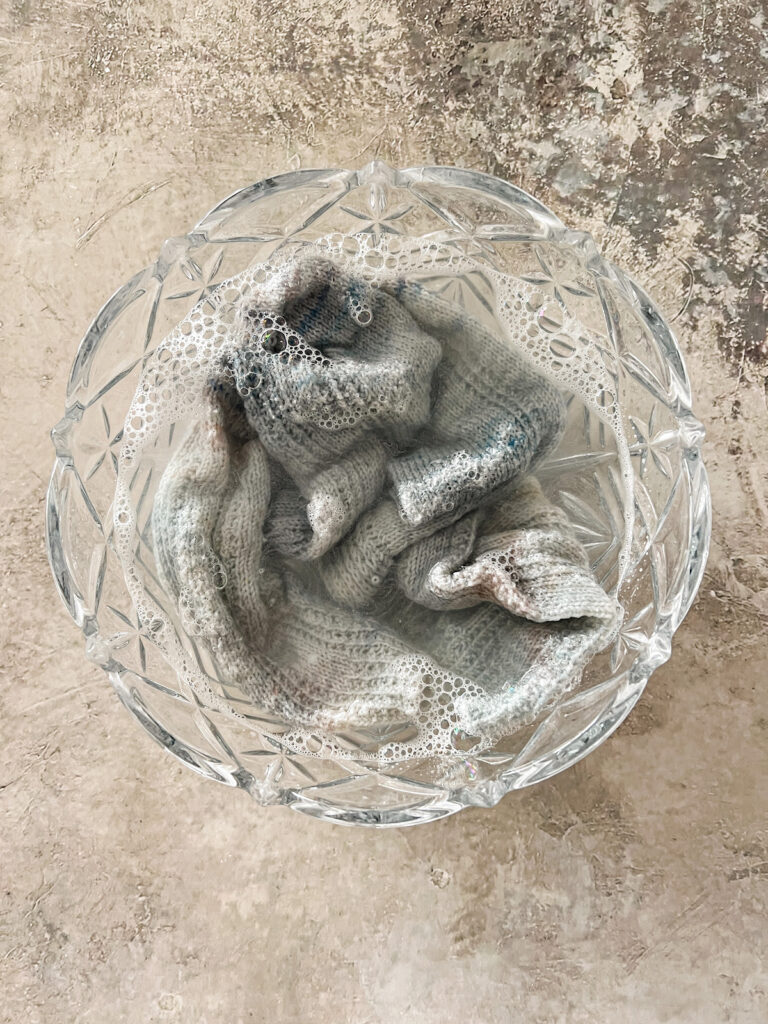 A glass bowl full of water and two light blue socks soaking in the water.