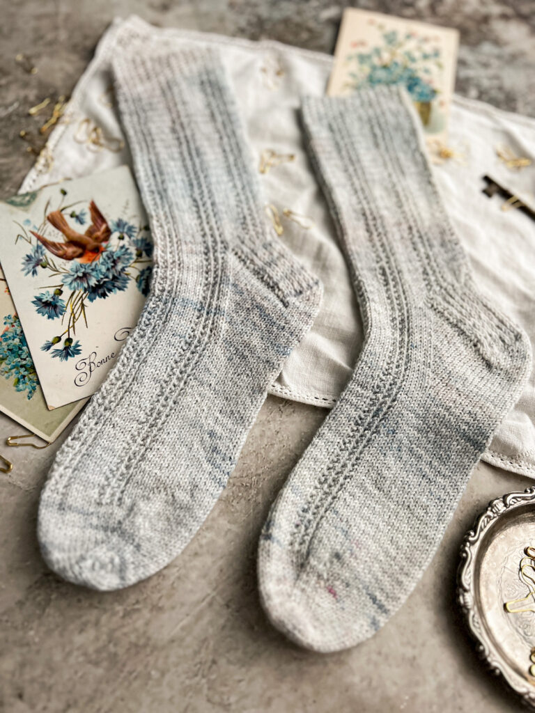 A close-up on the feet of a pair of light blue knit socks with purl columns running the length of the socks. The toes are pointing to the left.