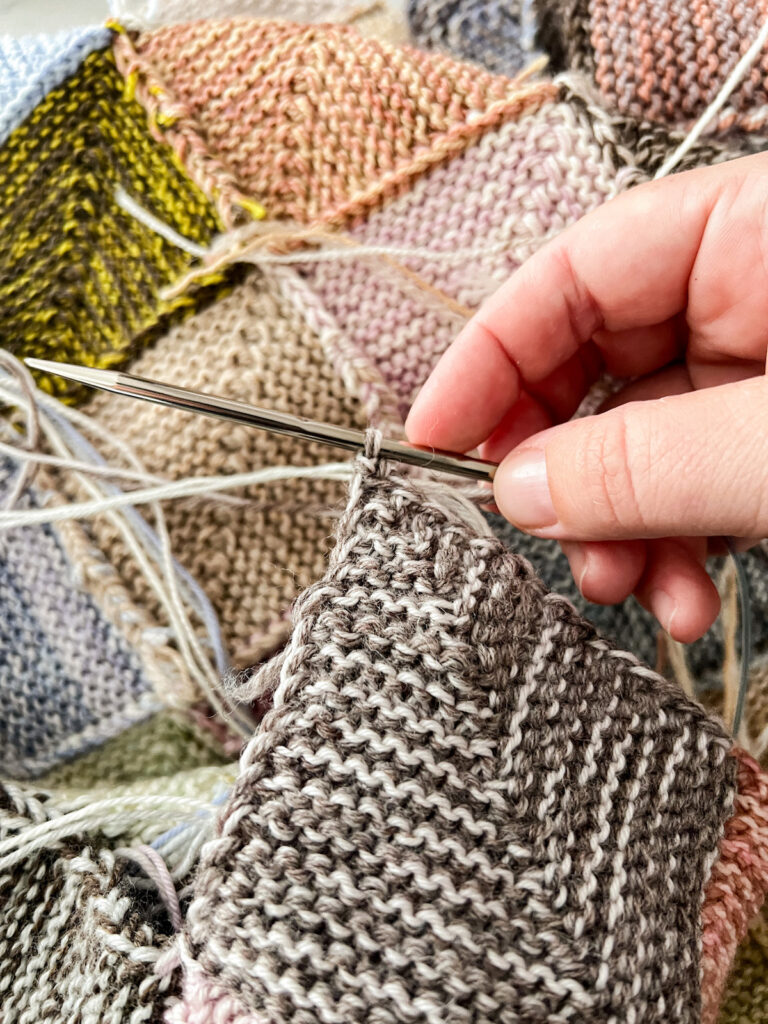 A close up on a brown and white mitered square, showing how at the end of the square, one stitch will remain on the right-hand needle.