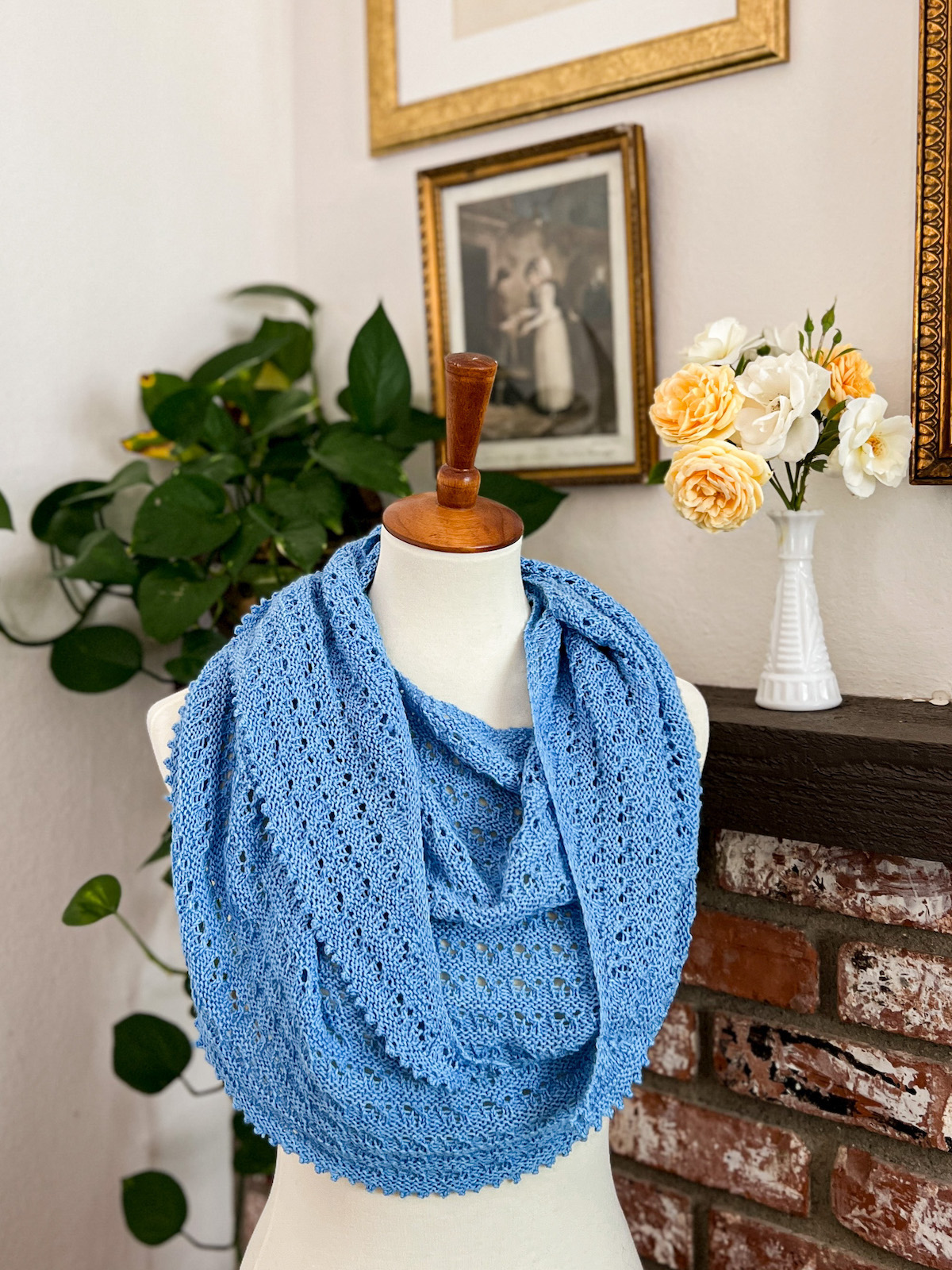 A light blue, crescent-shaped shawl is draped around a white dressmaker's form. The shawl has stripes with eyelet texture and stripes of garter stitch.