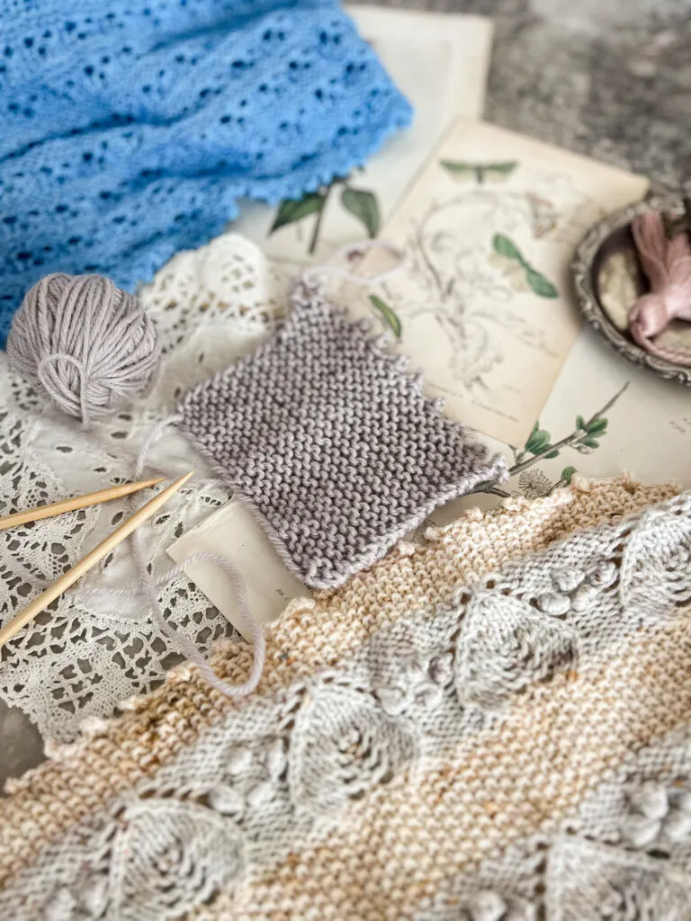 A gray garter stitch swatch with a picot bind-off sits between two shawls that also have picot bind-offs. They are surrounded by antique paper ephemera.