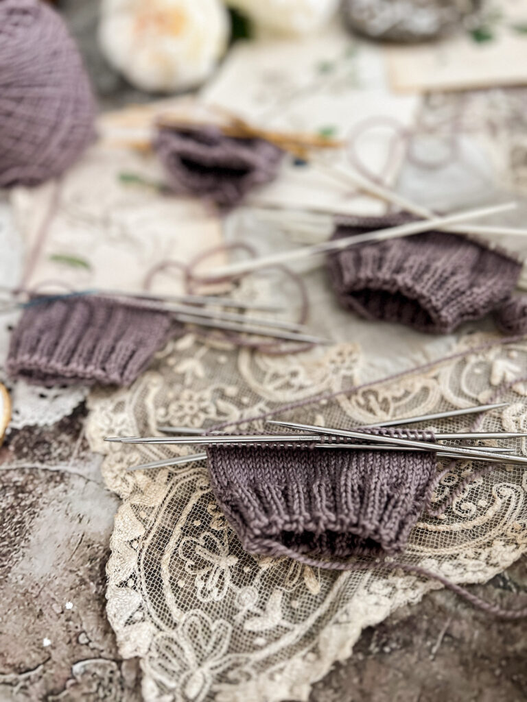 A photo taken from a low angle showing four swatches of yarn knit on four different sets of double pointed needles. The photo is focused on the lower right quadrant, which shows a swatch knit with ChiaoGoo steel double pointed needles.