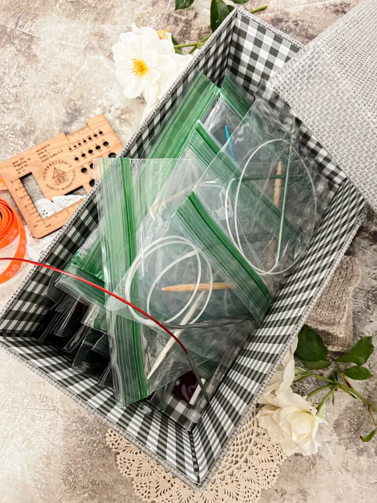 A top-down photo of a rectangular box with a plaid print on the interior walls. It is filled with ziploc bags, each of which has a set of circular needles inside.