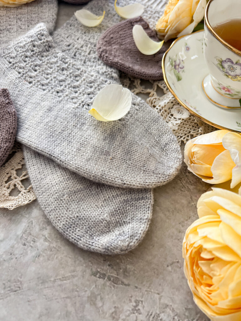 A close-up on the toes of a pair of light blue-gray handknit socks. These socks feature round toe construction, which is a roomier toe than the usual wedge toe.