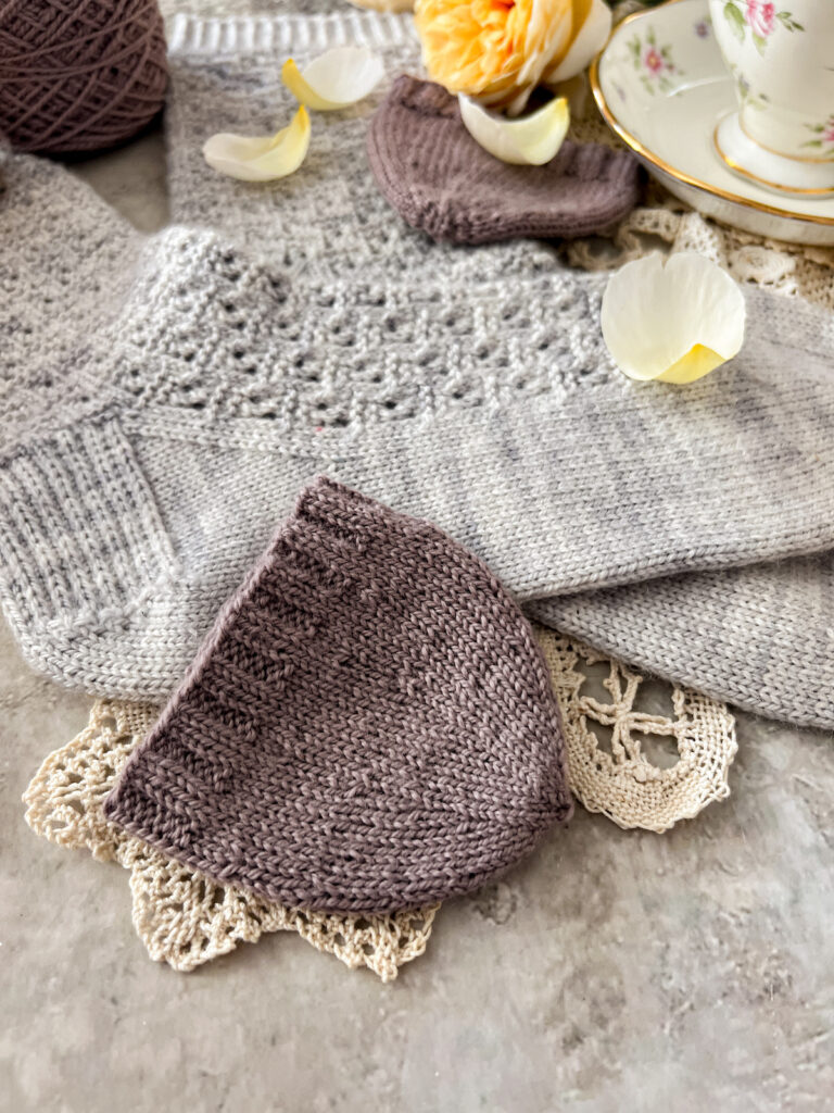 A close-up on a purple knit swatch of a round toe knit from the cuff down. This shows how the decreases stack up as the toe decreases in circumference. Blurred slightly in the background are a pair of light blue-gray handknit socks.