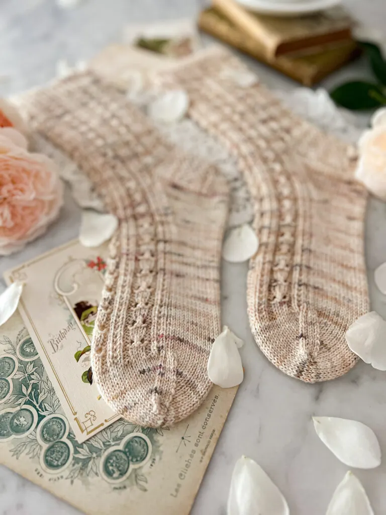 A pair of lightly speckled, pale pink socks is laid flat on a white marble countertop. This photo, taken from a low angle, shows the toes of the socks while the rest is blurred in the background.