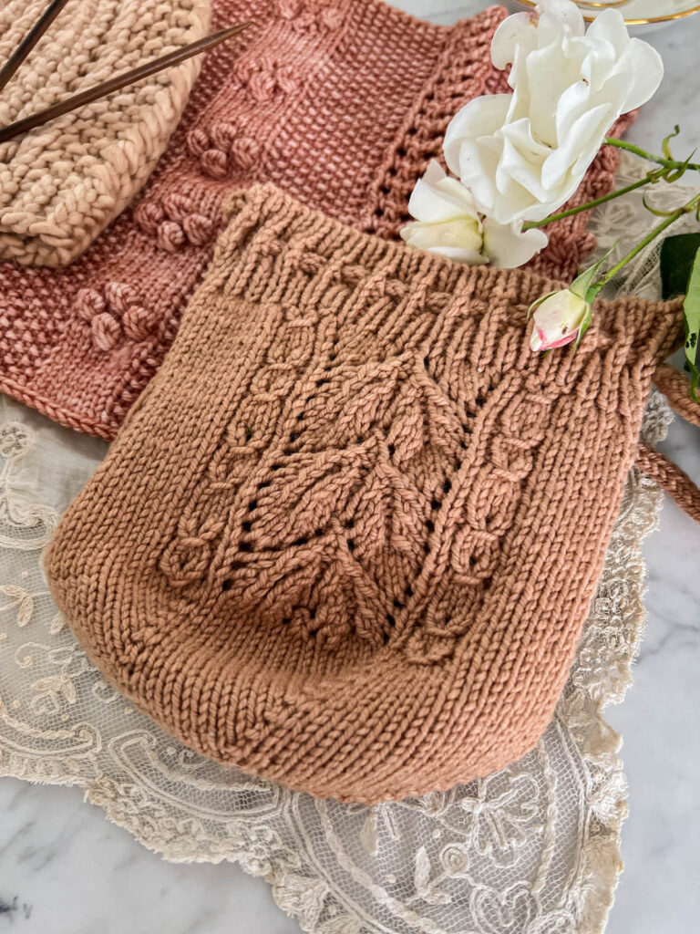 A pink tea cozy with lacy leaves down the side is laid flat on a white marble countertop and photographed from a low angle.