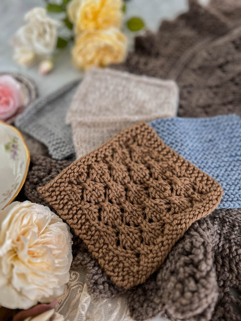 A brown swatch of simple lace fabric is laid flat on top of several other swatches and surrounded by yellow and cream roses.