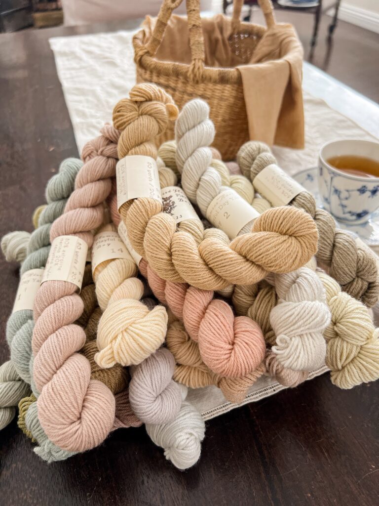 A pile of pastel mini skeins of yarn sits on a dark brown coffee table.