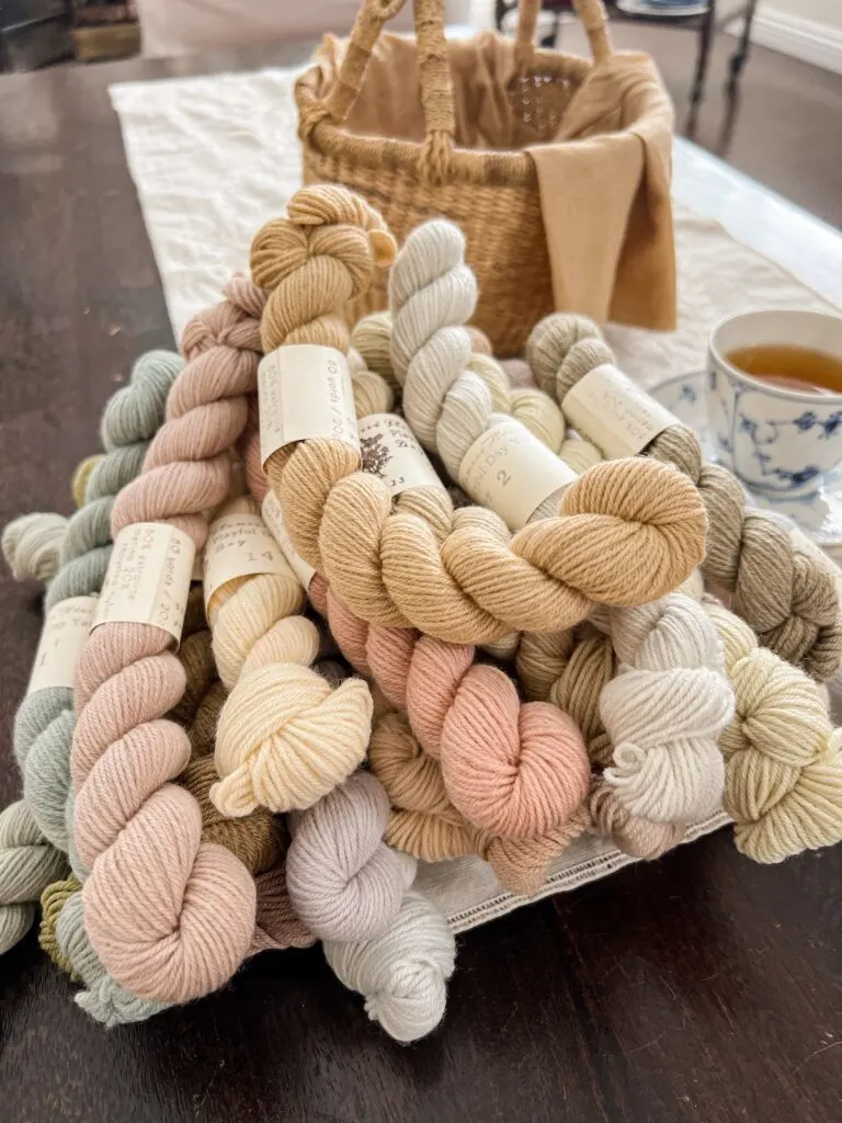 A pile of pastel mini skeins of yarn sits on a dark brown coffee table.