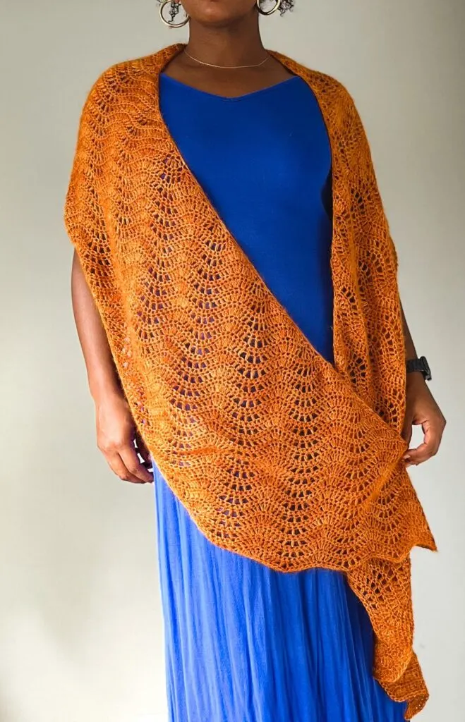 A Black woman in a long blue dress stands with an orange lacy wrap draped around her shoulders.