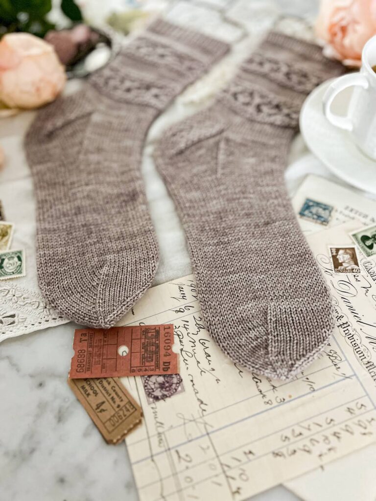 A close-up on the toes of a pair of handknit gray socks. This image shows that the toes are knit with a whimsical star toe construction.